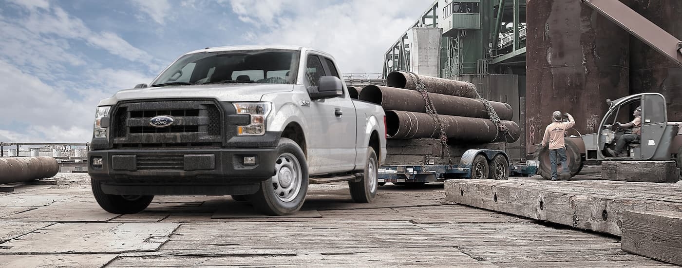 White 2015 Ford F-150 towing a pallet of pipes at a worksite.