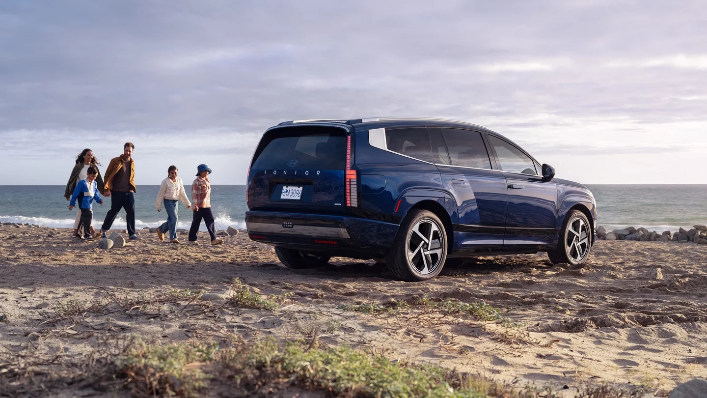 A blue Hyundai IONIQ 9 parked on a beach with a family walking towards it