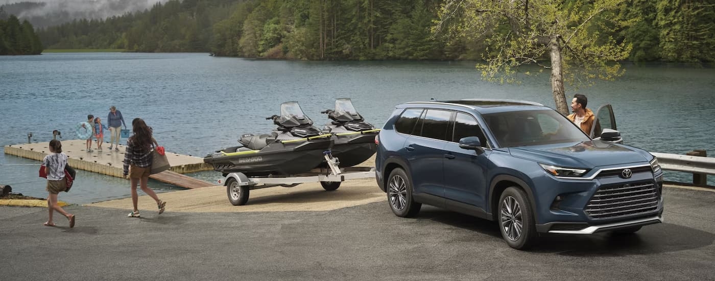 Blue 2026 Toyota Grand Highlander towing jet skis near a lake