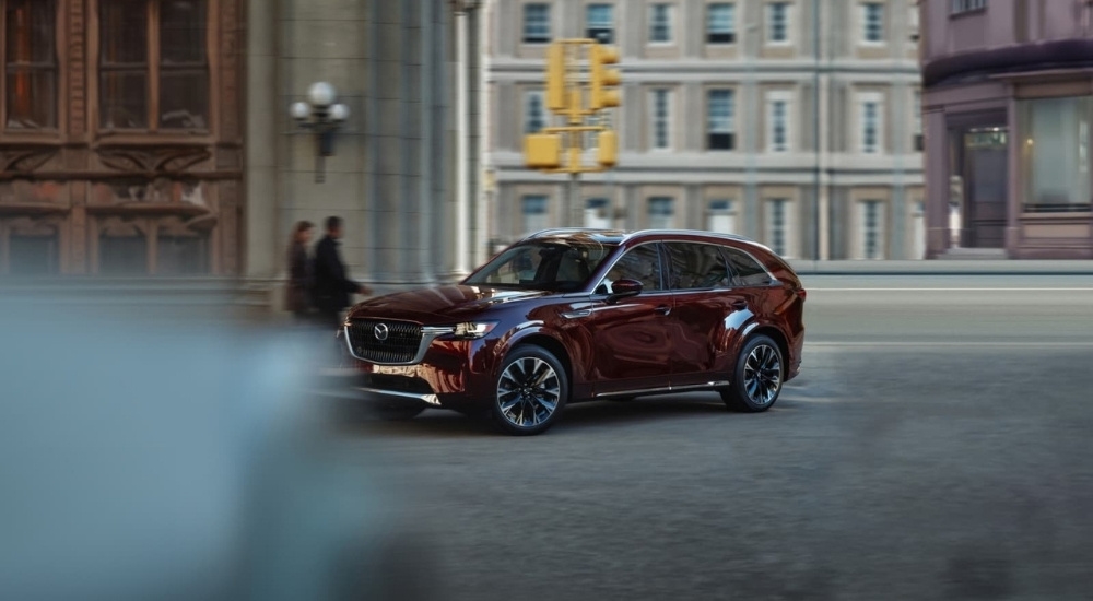 Red 2026 Mazda CX-90 Hybrid driving down a road.