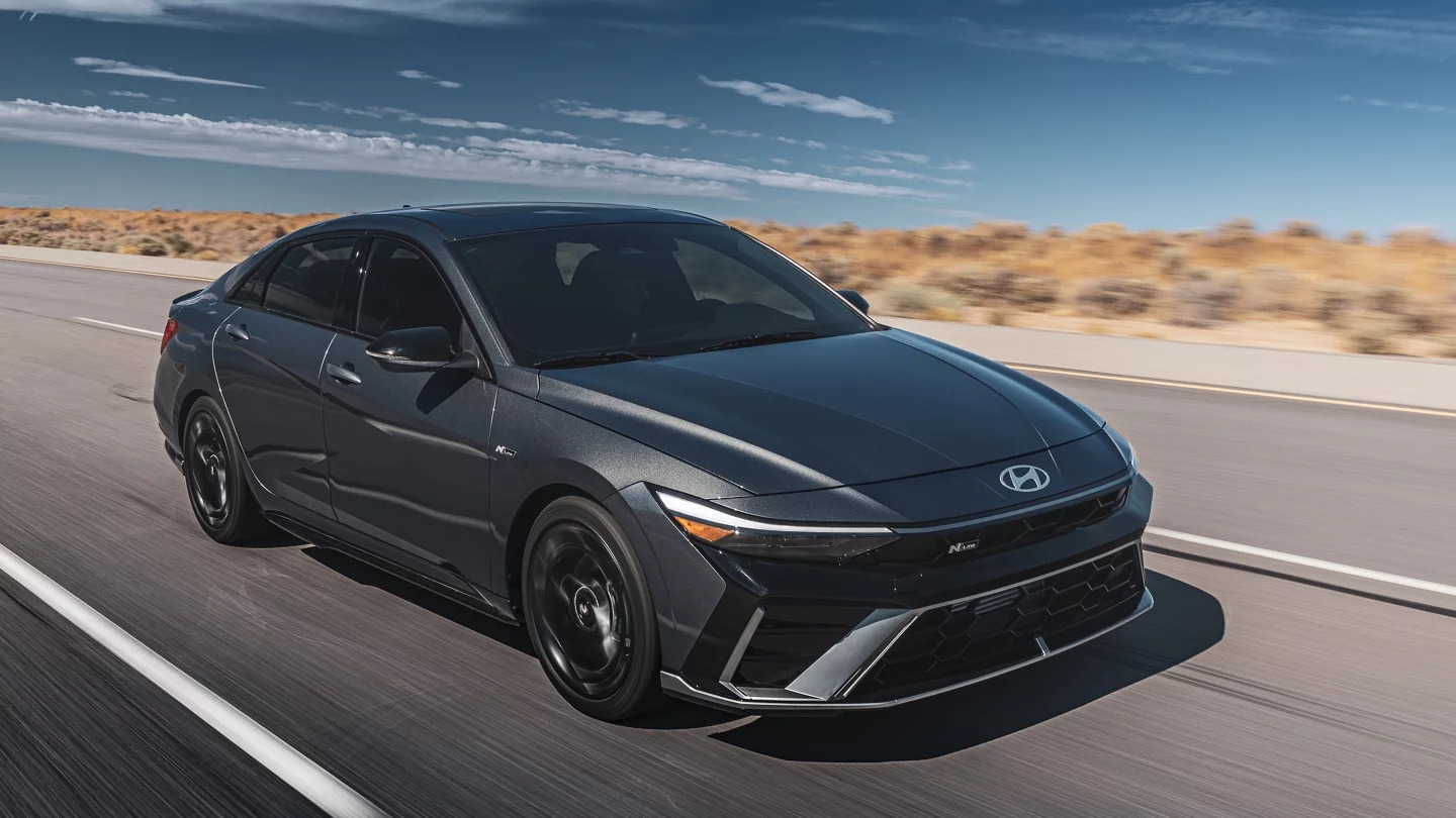 A black Hyundai Elantra driving quickly down the road through a
desert.