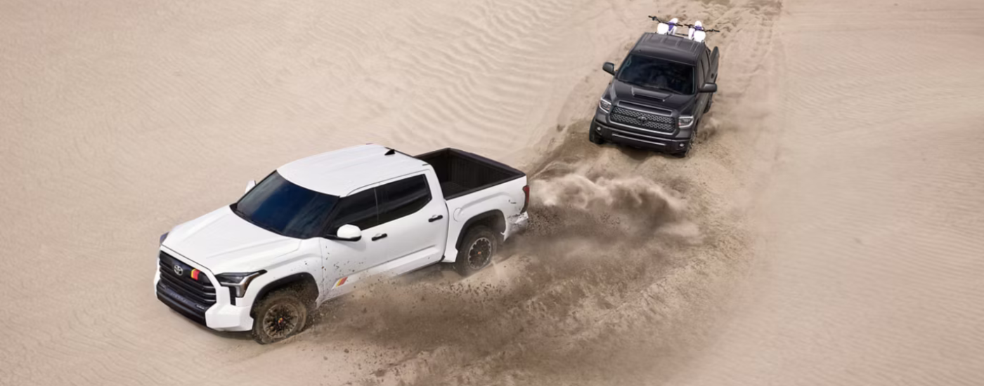 White 2026 Toyota Tundra TRD Rally leading a black 2026 Toyota Tundra through a sand dune