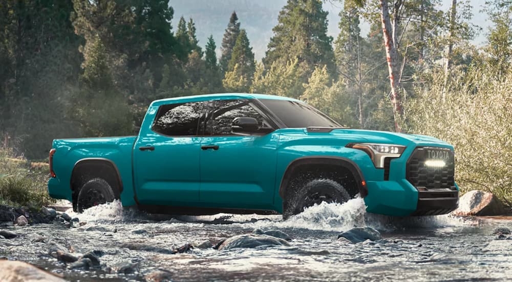 Side of a blue 2026 Toyota Tundra driving through a shallow river.
