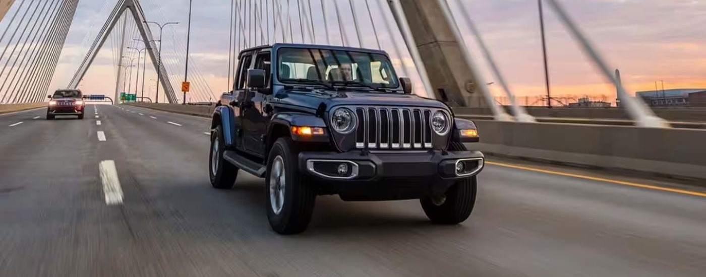 Black 2023 Jeep Wrangler driving over a bridge