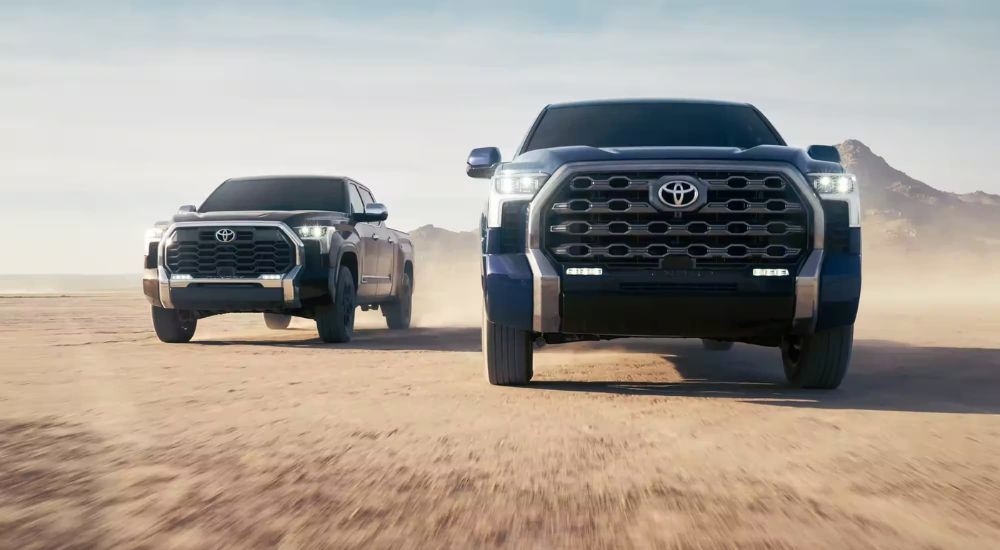 A blue 2026 Toyota Tundra and a silver 2026 Toyota Tundra i-Force Max driving in a desert