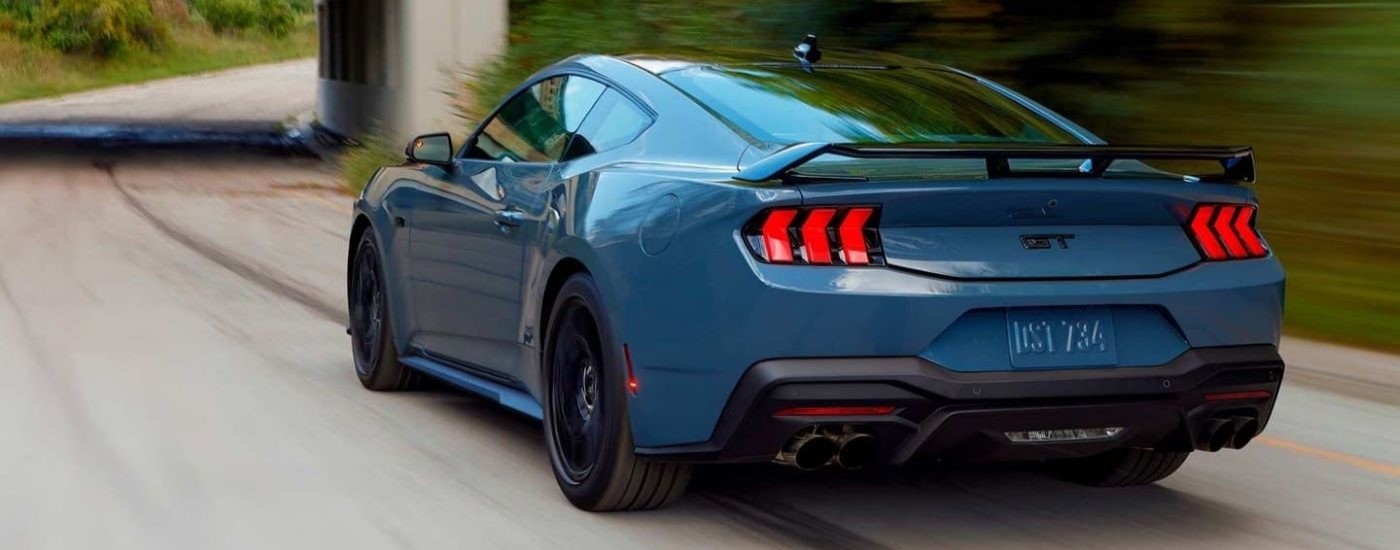 Rear of a blue 2026 Ford Mustang GT driving down a road.