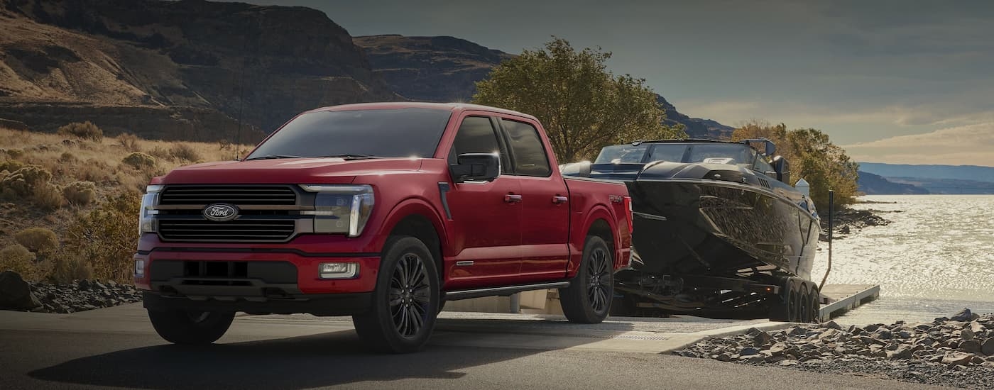 Red 2026 Ford F-150 STX towing a boat out of lake.