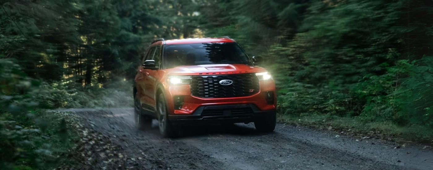 Red 2026 Ford Explorer driving off-road through a forest.