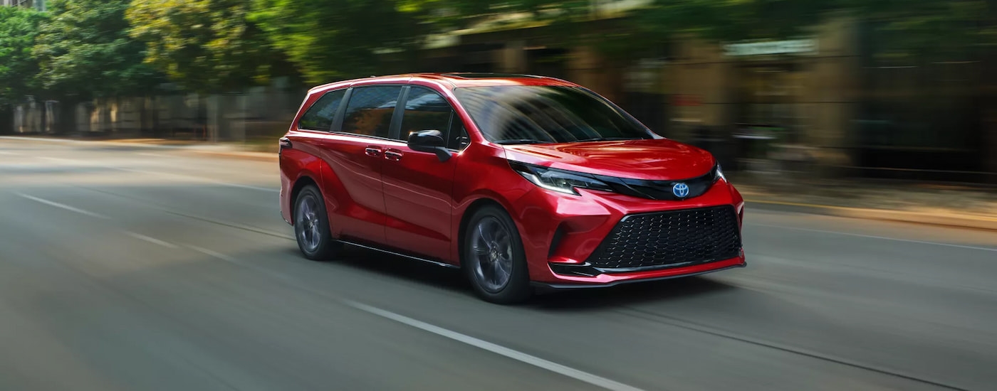 Red 2025 Toyota Sienna driving down a road.