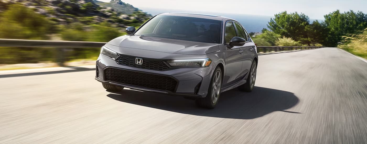 Grey 2026 Honda Civic driving down a road.