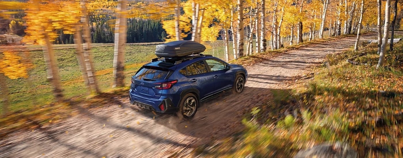 Blue 2024 Subaru Crosstrek driving on a tree-lined trail