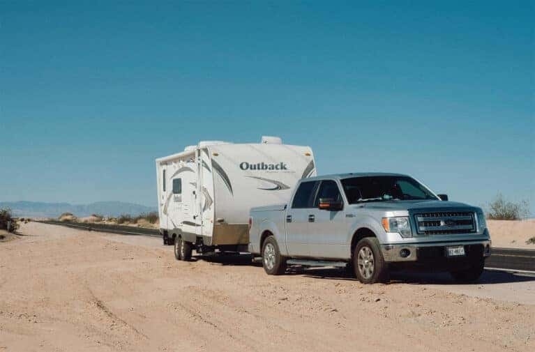 Silver Ford truck towing a white trailer in the desert