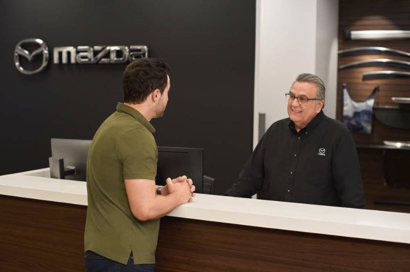 Service advisor at a desk talking with a customer under a Mazda wall logo