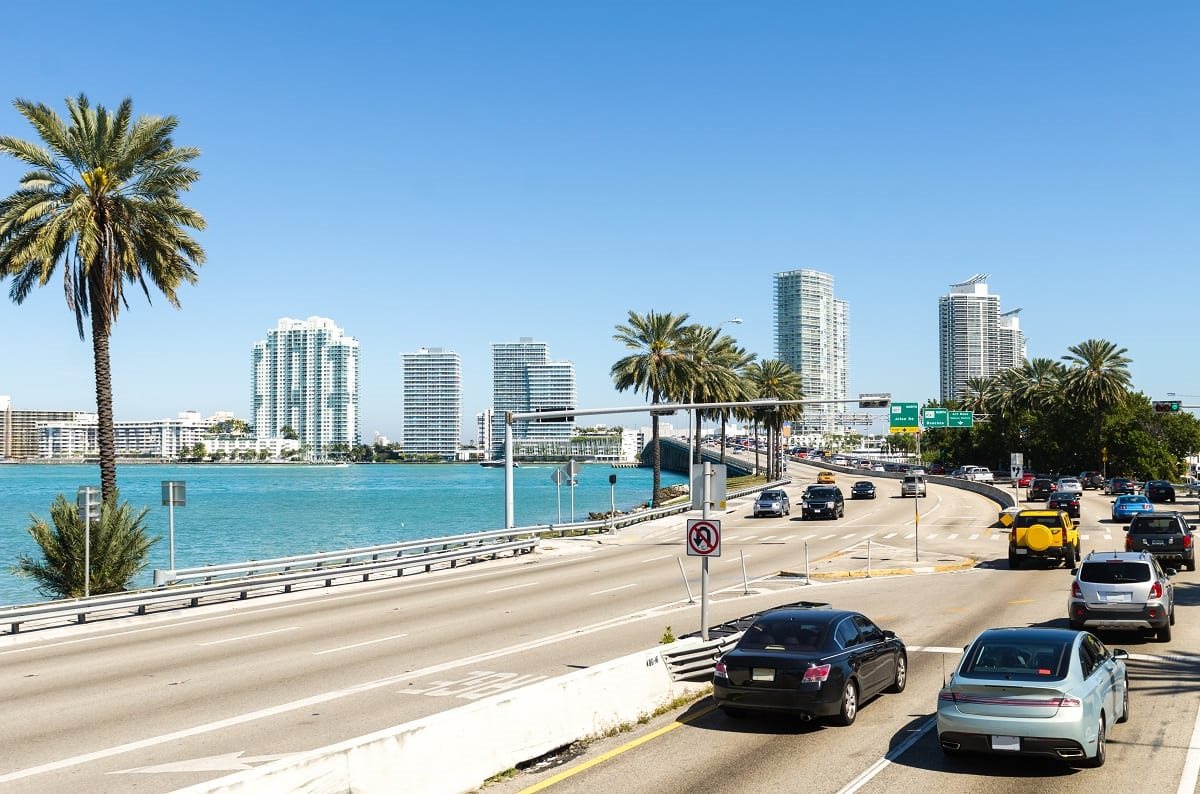 Traffic on a palm-lined Miami causeway with downtown towers behind