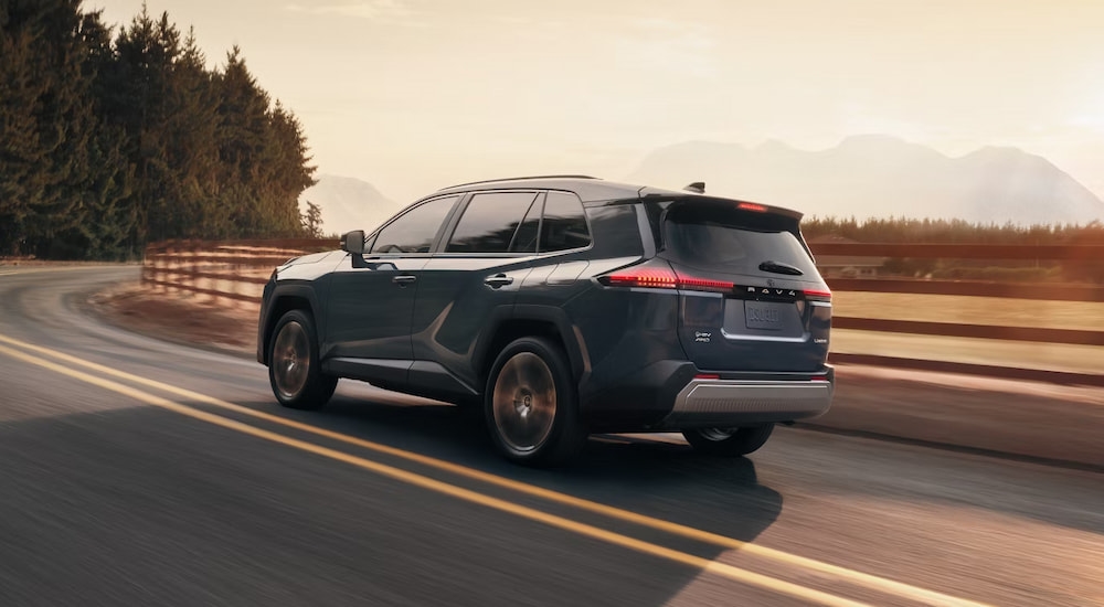 Rear of a dark blue 2026 Toyota RAV4 driving down a winding road.