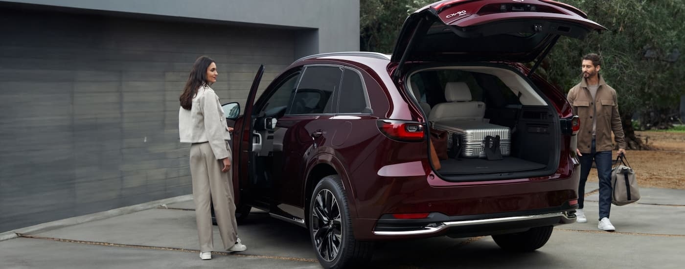 Man and a woman putting a bag into the back of a maroon 2026 Mazda CX-90