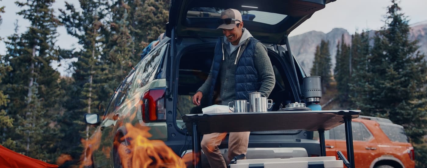 Man camping and cooking food next to a green 2026 Honda Passport