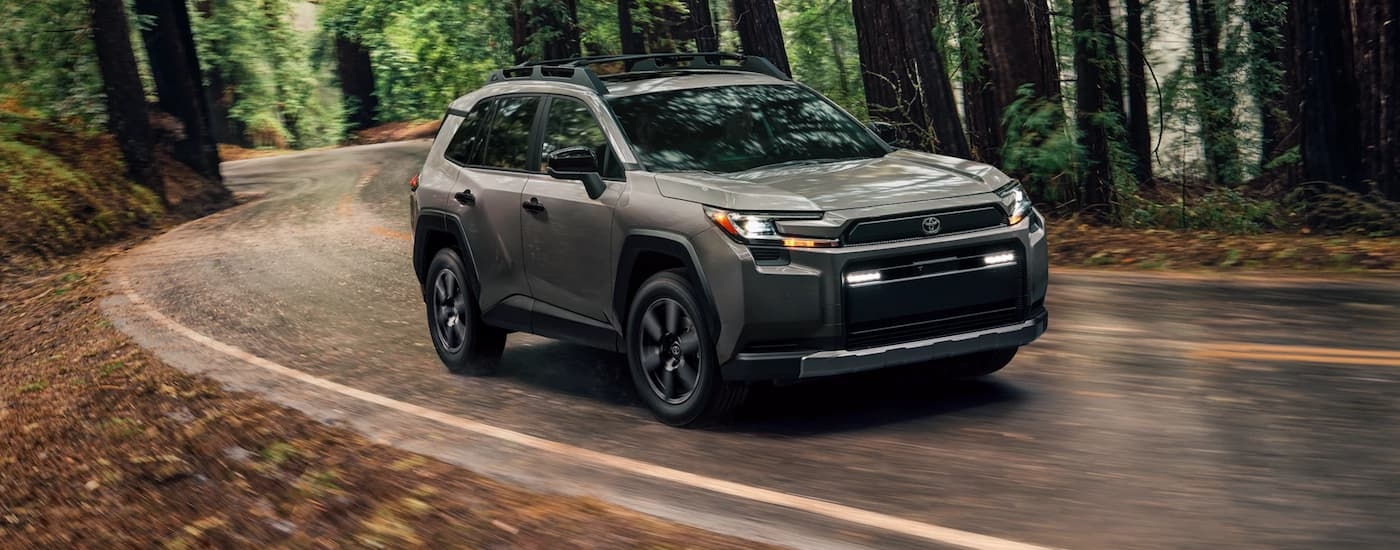 Grey 2026 Toyota RAV4 driving down a forest road.
