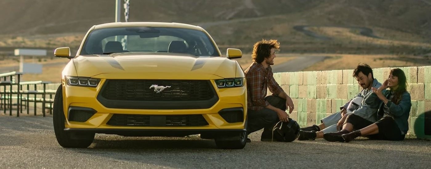 People sitting near a parked yellow 2024 Ford Mustang 
