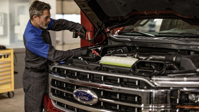 Ford technician performing maintenance under the hood of a truck engine