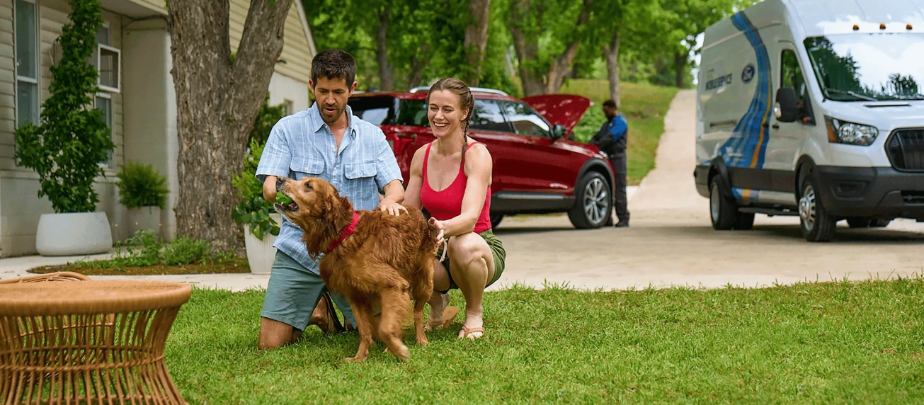 Ford Mobile Service technician working on vehicle at home while customers relax outside with their dog