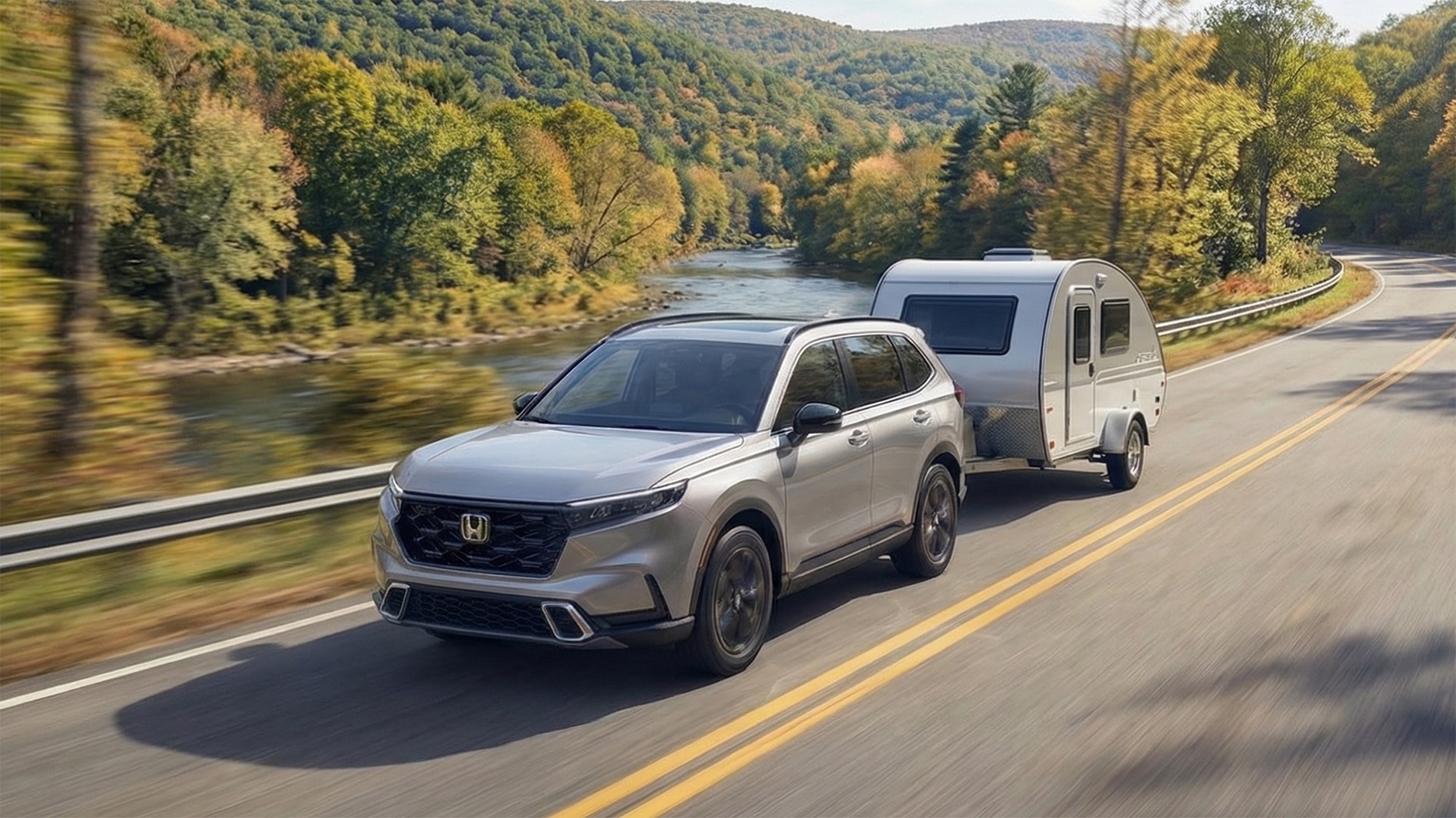 Silver 2026 Honda CR-V towing a compact teardrop camper along a winding two-lane road beside a river, surrounded by early fall foliage and rolling Catskills hills.