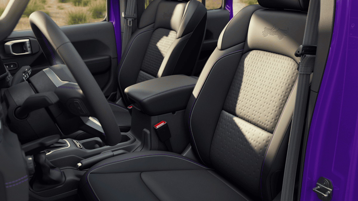 2026 Jeep Wrangler interior seating in Margate FL with black and tan two-tone perforated cloth front seats, purple accent stitching, and center console armrest