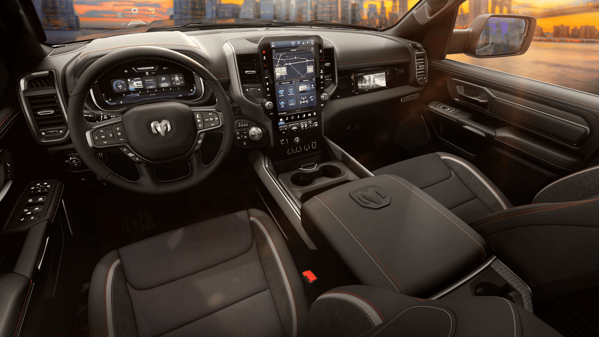 2026 Ram 1500 interior in Margate FL showing Ram-branded steering wheel, large vertical touchscreen with navigation, digital instrument cluster, and black leather seats with orange accent stitching