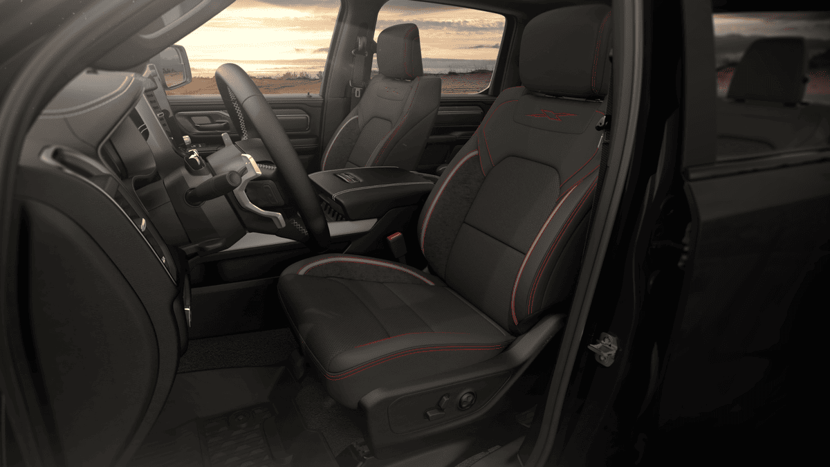 2026 Ram 1500 front seat interior in Margate FL with black leather seating and red contrast stitching, center console armrest, and sport steering wheel at sunset