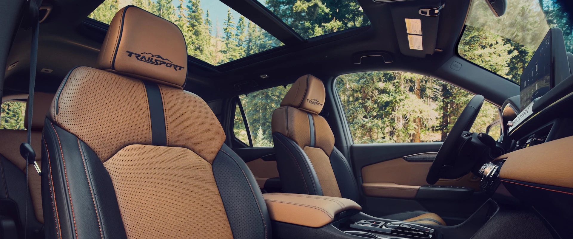 2026 Honda Passport TrailSport Elite interior with brown perforated leather seats, contrast stitching, TrailSport logo headrests, panoramic sunroof, and modern dashboard layout surrounded by a forest setting