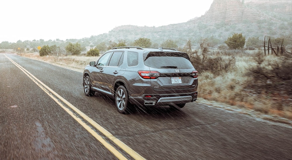 Rear of a grey 2026 Honda Pilot driving down an open road.
