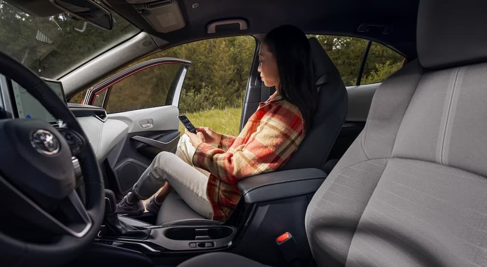 Woman on her phone sitting in the passenger seat in a 2026 Toyota Corolla