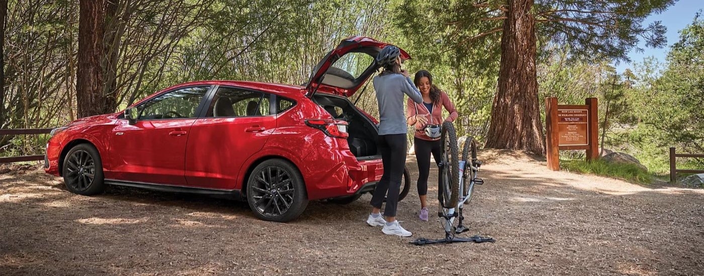 Rear of a red 2025 Subaru Impreza RS parked off-road in a forest.