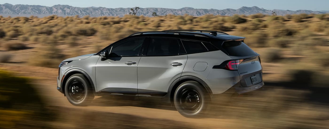 Side of a silver 2026 Kia Sportage driving off-road.