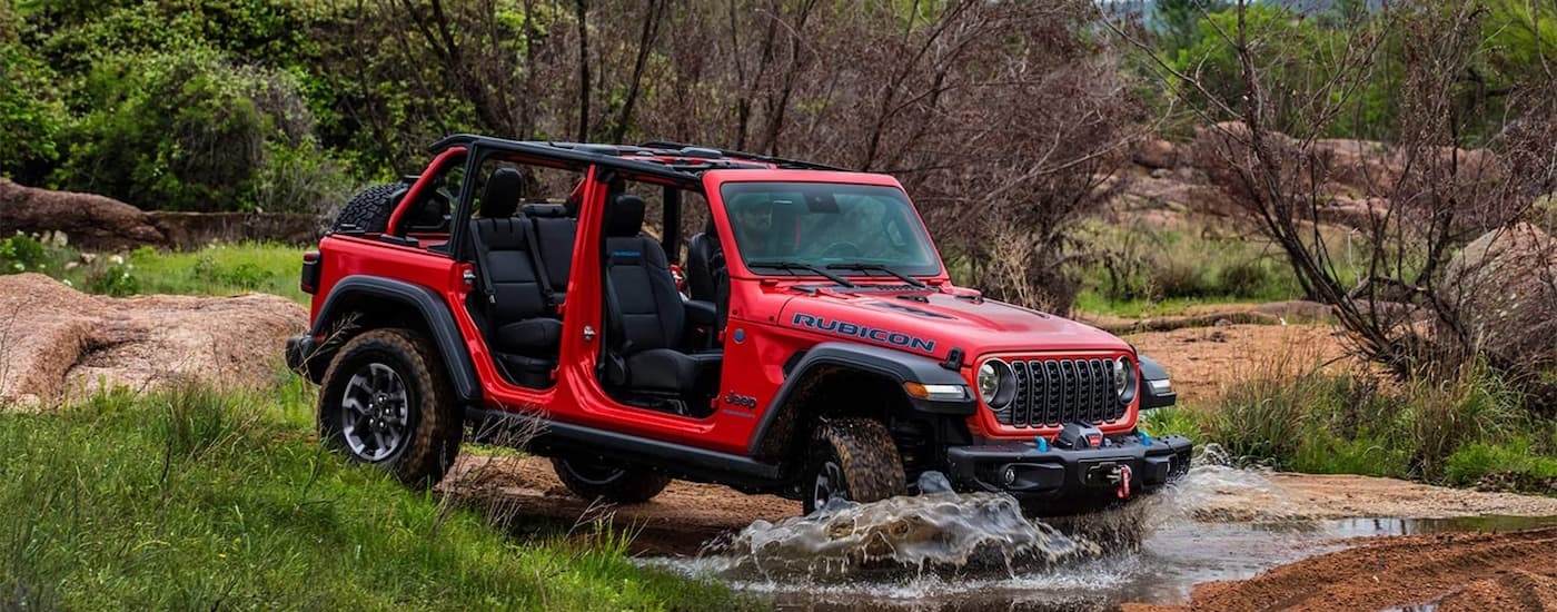 Red 2026 Jeep Wrangler Rubicon driving off-road near a river.