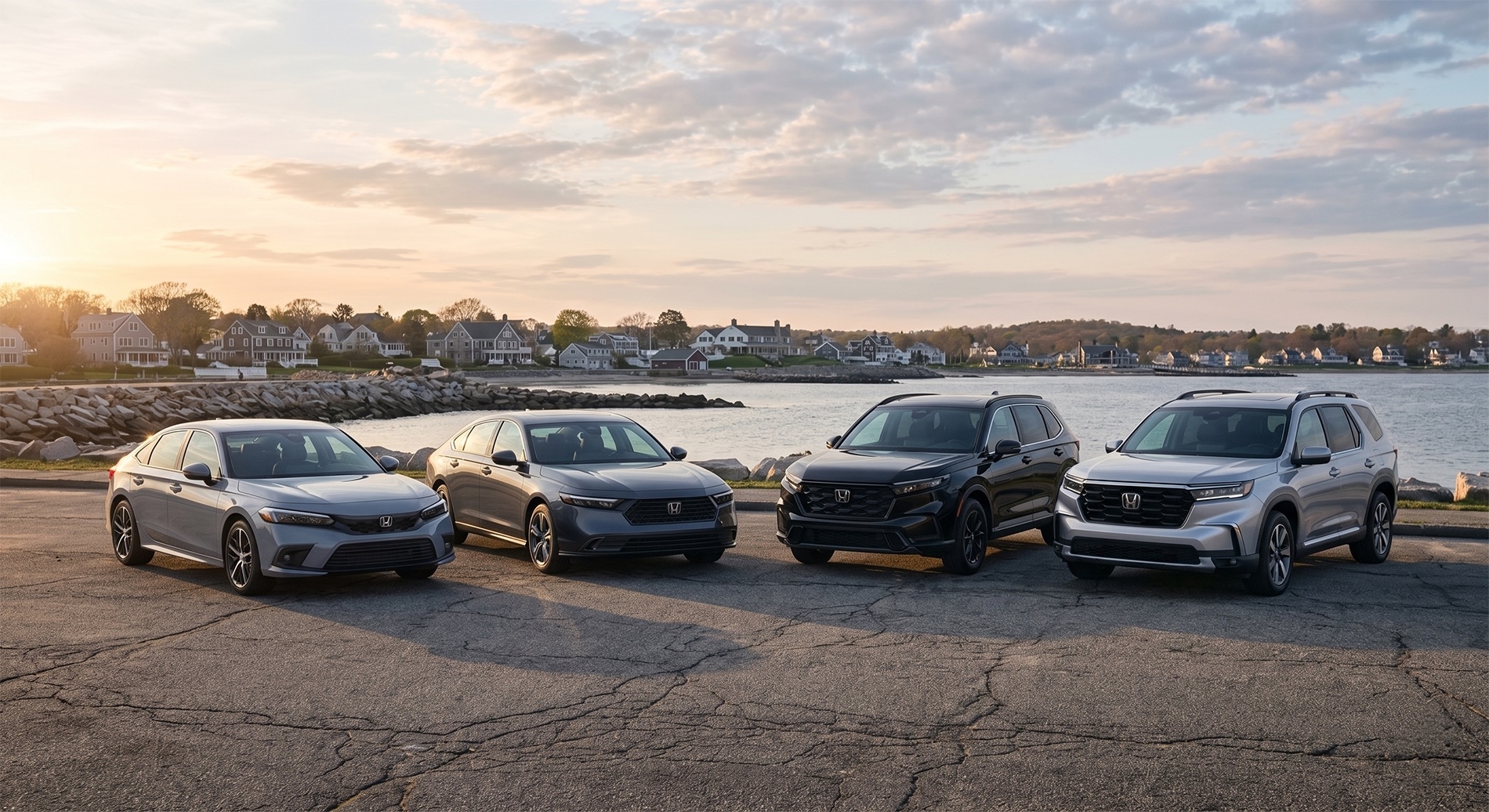 2026 Honda Civic, Accord, CR-V, and Pilot parked in a staged lineup along a South Coast Massachusetts shoreline at sunset, with cracked asphalt in the foreground, rocky seawall and calm water behind, and coastal homes under a soft golden-hour sky