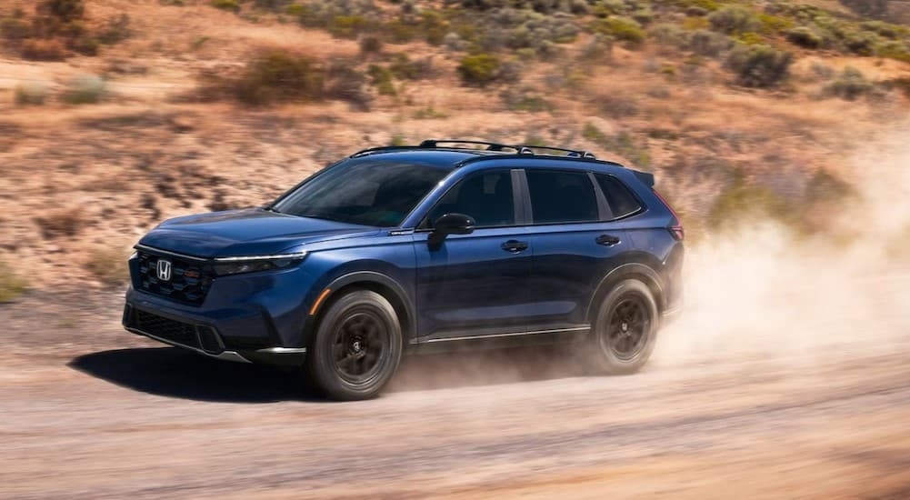 A blue 2026 Honda R-VHybrid driving on a dirt road.