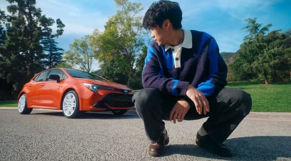 A person near an orange 2026 Toyota Corolla Hatch.