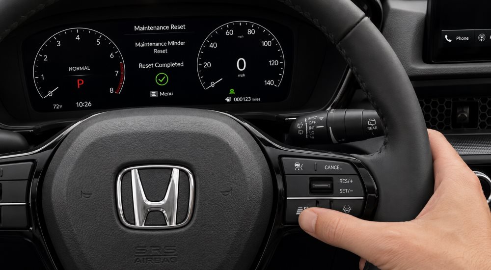 Hand using Honda steering wheel controls to reset Maintenance Minder