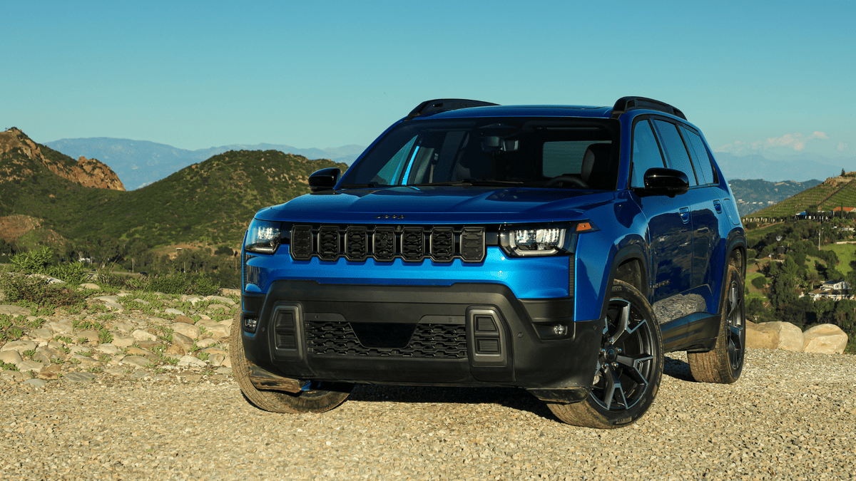 2026 Jeep Cherokee in Margate FL in hydro blue with seven-slot grille, LED headlights, black roof rails, and dark alloy wheels on a gravel overlook with mountain backdrop