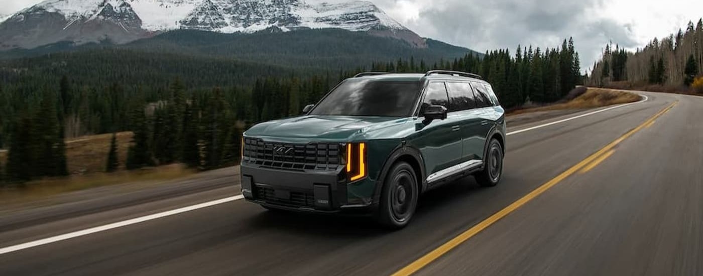 A green 2027 Kia Telluride driving on a highway.
