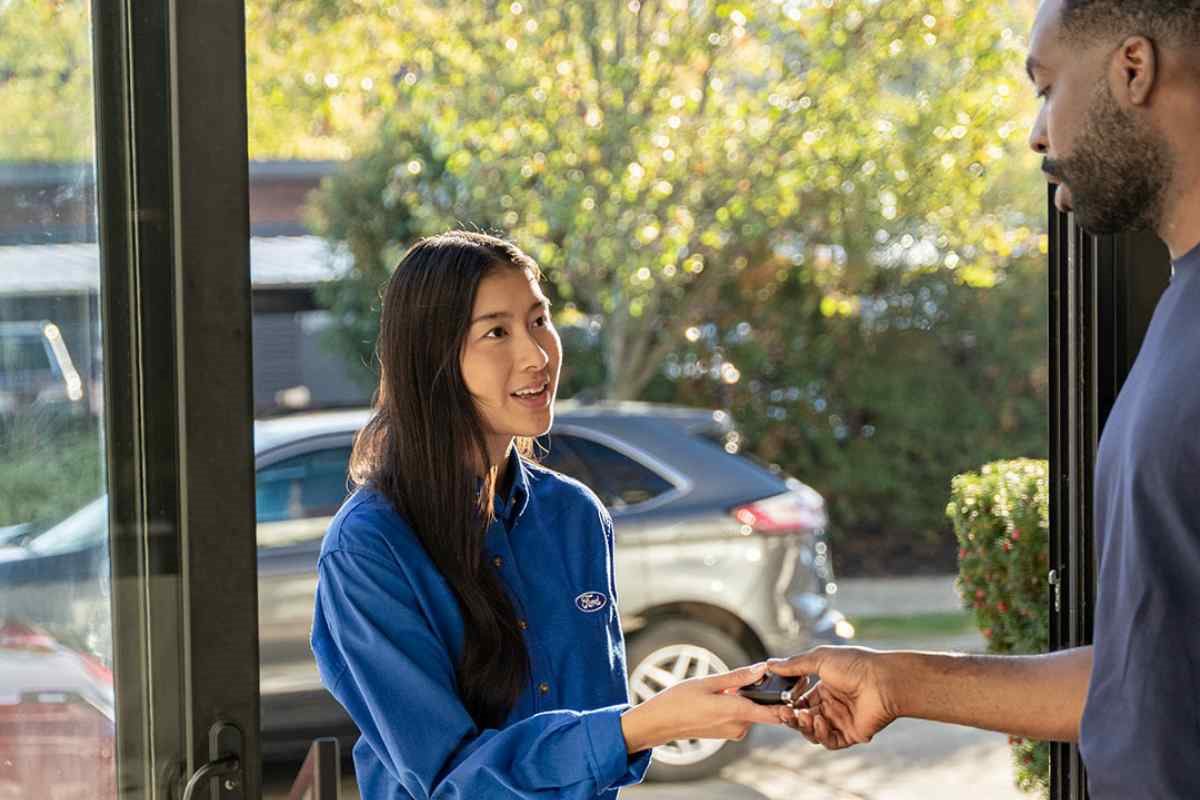 Ford service representative handing vehicle keys to a customer at home, representing convenient Ford Pickup & Delivery service for dealership maintenance.