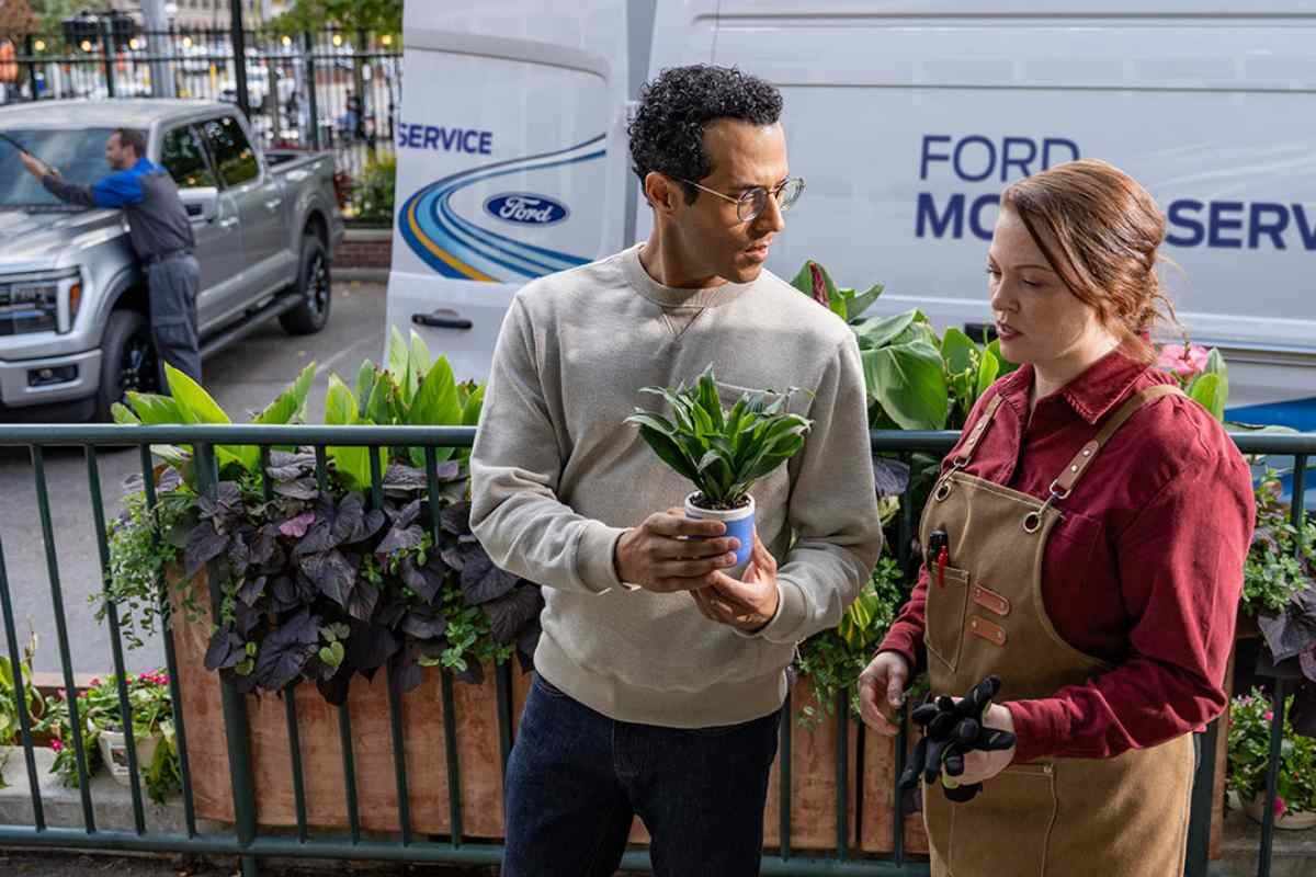 Ford Mobile Service technician speaking with a customer beside a Ford Mobile Service van while a Ford truck receives service nearby, representing convenient on-site vehicle maintenance.