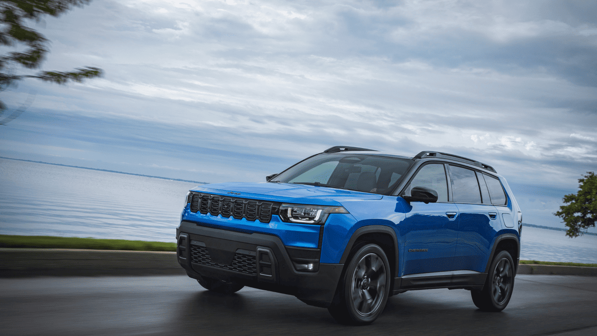2026 Jeep Cherokee in Margate FL in blue with seven-slot grille, LED headlights, black roof rails, and black wheels driving along a coastal waterfront road — a capable SUV alternative to the Nissan Rogue