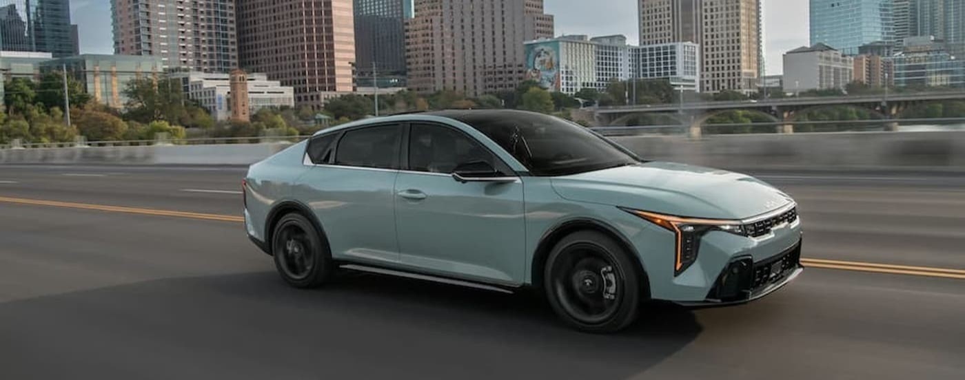 A blue 2026 Kia K4 driving near a city.