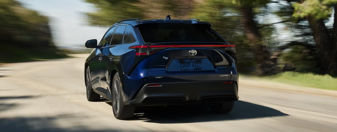 Rear of a dark blue 2026 Toyota bZ driving down a road.