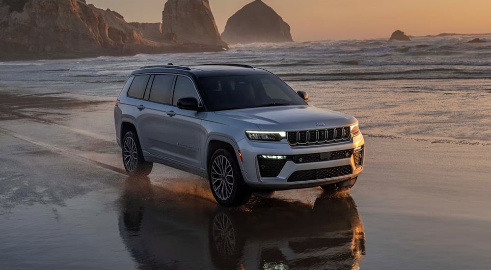 White 2026 Jeep Grand Cherokee driving near a lake.