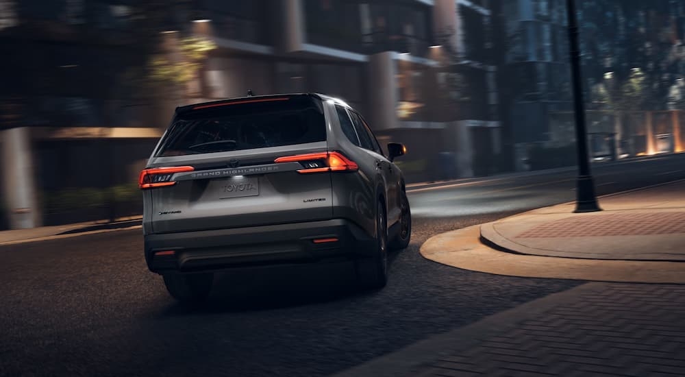 Rear of a grey 2026 Toyota Grand Highlander driving around a bend.