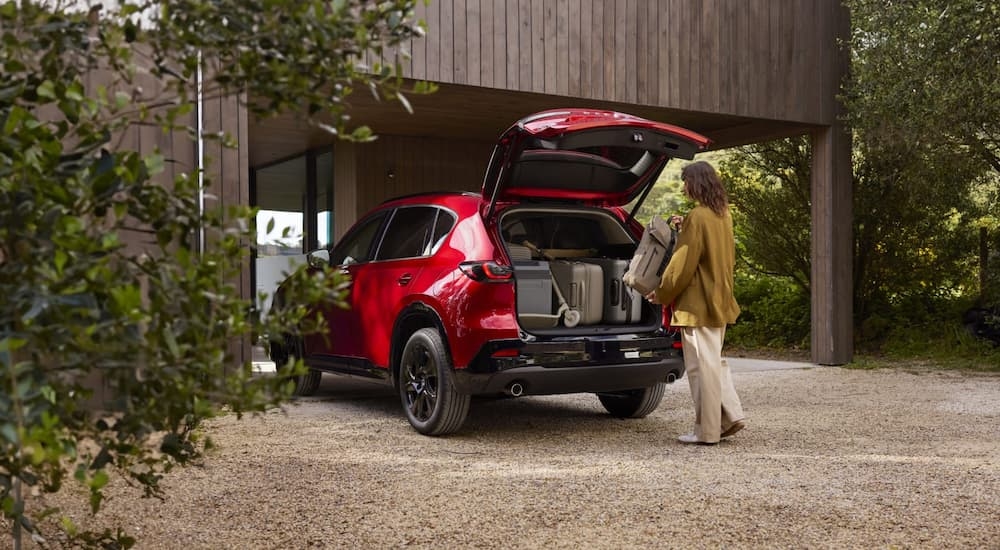 Person loading bags into the open hatch of a red 2026 Mazda CX-5.