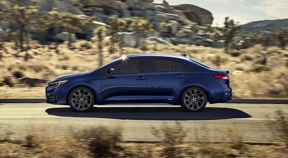 Side of a dark blue 2026 Toyota Corolla driving down an open road.